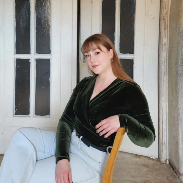 Die Galeristin sitzt in einem hellen Raum mit Flügeltür und Buntglasfenster im Jugendstil. Die Tür verbindet die Galerieräume miteinander.