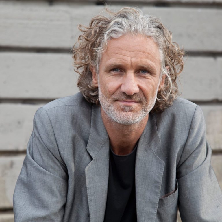 Ein Profilfoto des Künstlers Martin Bruno Schmid. Er sitzt im Außenbereich und schaut in die Kamera.